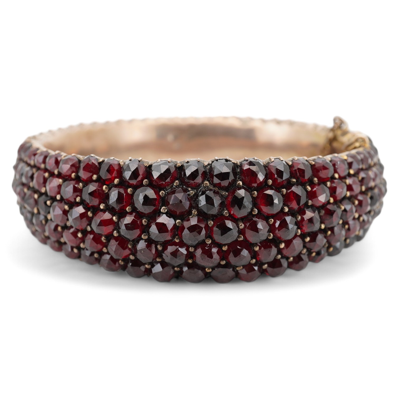 An Edwardian yellow metal overlaid and facetted garnet cluster set hinged bracelet, with safety chain, interior diameter 59mm. Condition - poor to fair